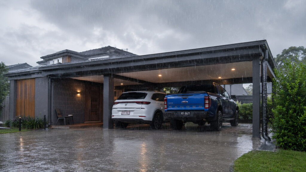 Insulated carport protecting two vehicles from heavy rain at a Robina home.